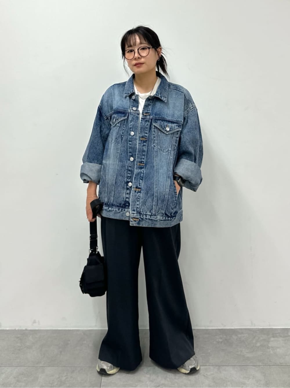 グレー系のスラックス、ブラック系のショルダーバッグ、ブルー系のデニムジャケットを着用したレディースの秋コーディネートの1枚目の写真