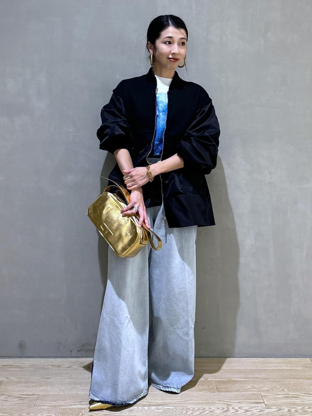 ゴールド系のショルダーバッグ、ブラック系のブルゾン、ホワイト系のTシャツ/カットソーを着用したレディースの秋コーディネートの1枚目の写真