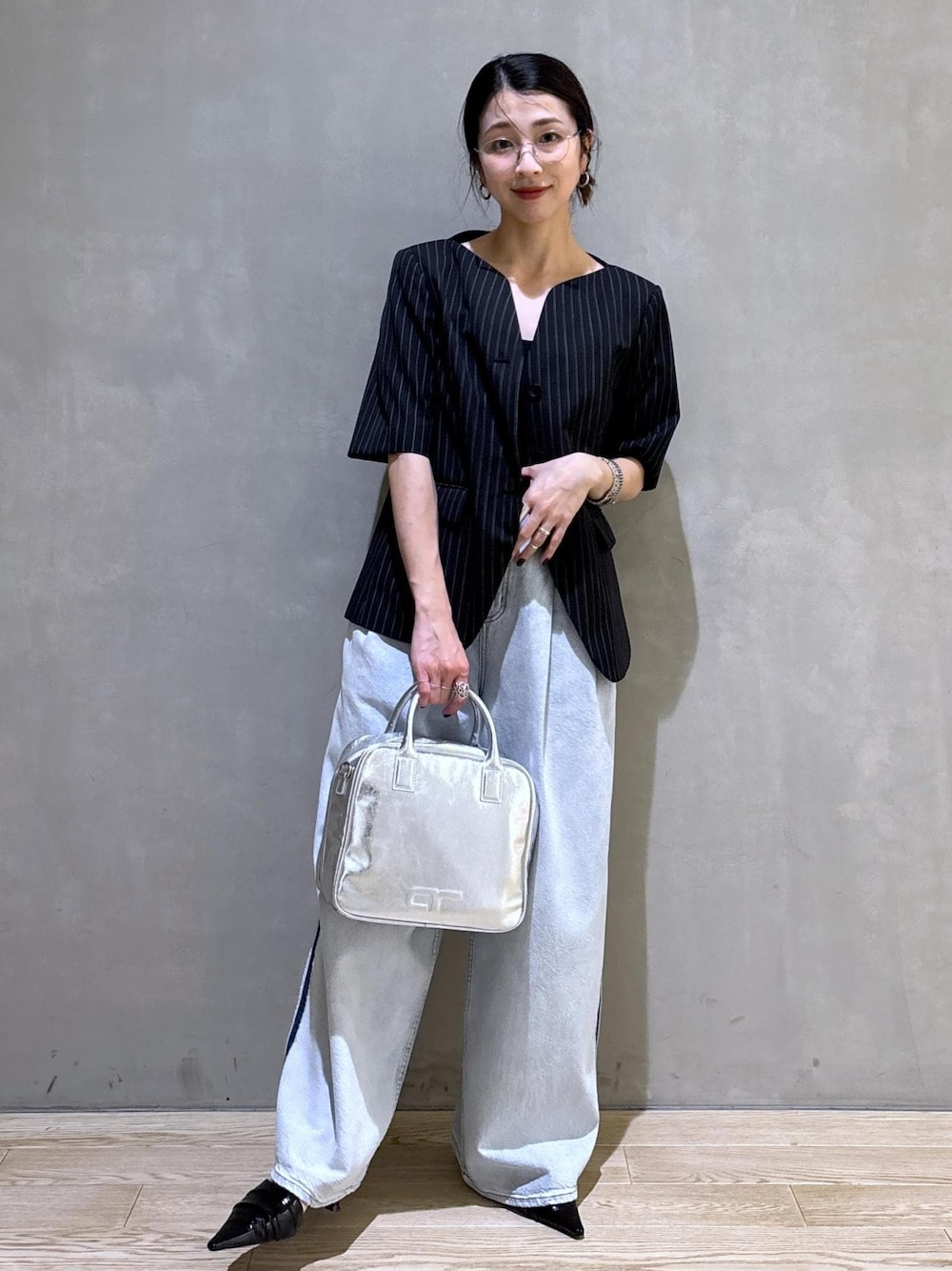 ブルー系のデニムパンツ、ブラック系のノーカラージャケット、シルバー系のボストンバッグを着用したレディースの春コーディネートの1枚目の写真
