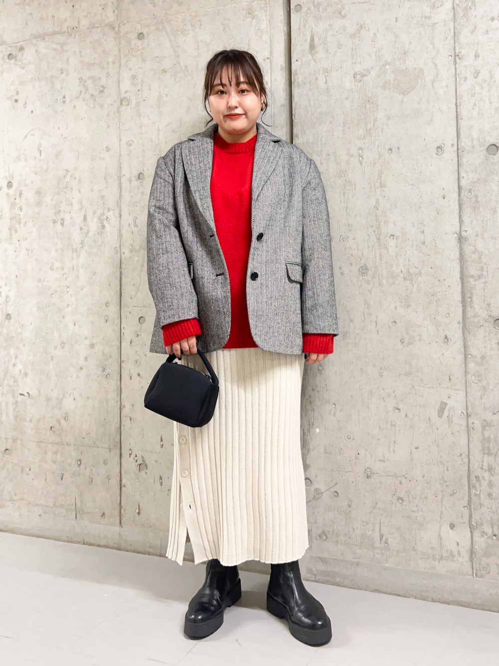 レッド系のニット/セーター、ブラック系のその他アウター、ベージュ系のスカートを着用したレディースの冬コーディネートの1枚目の写真