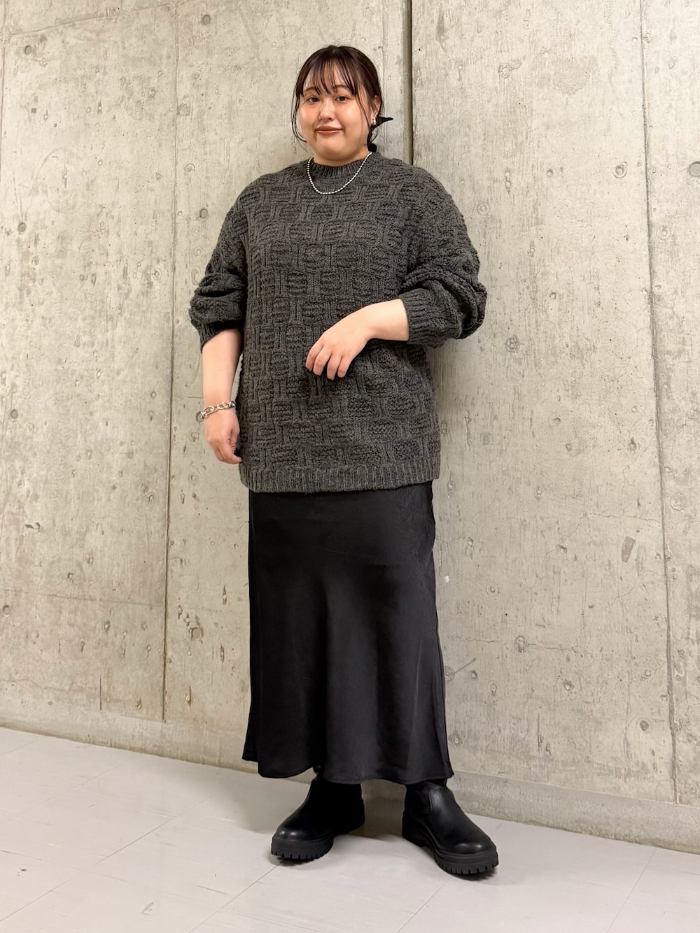 グレー系のニット/セーター、ブラック系のスカート、ブラック系のブーツを着用したレディースの冬コーディネートの1枚目の写真