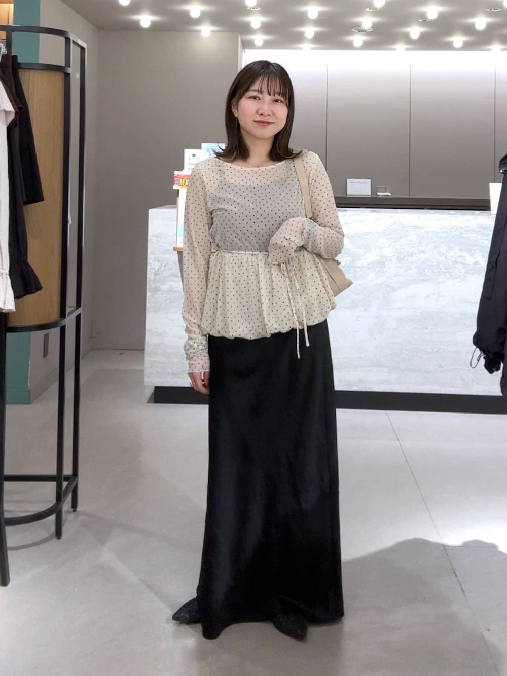 ブラック系のスカート、ベージュ系のショルダーバッグ、ブラック系のパンプスを着用したレディースの春コーディネートの1枚目の写真