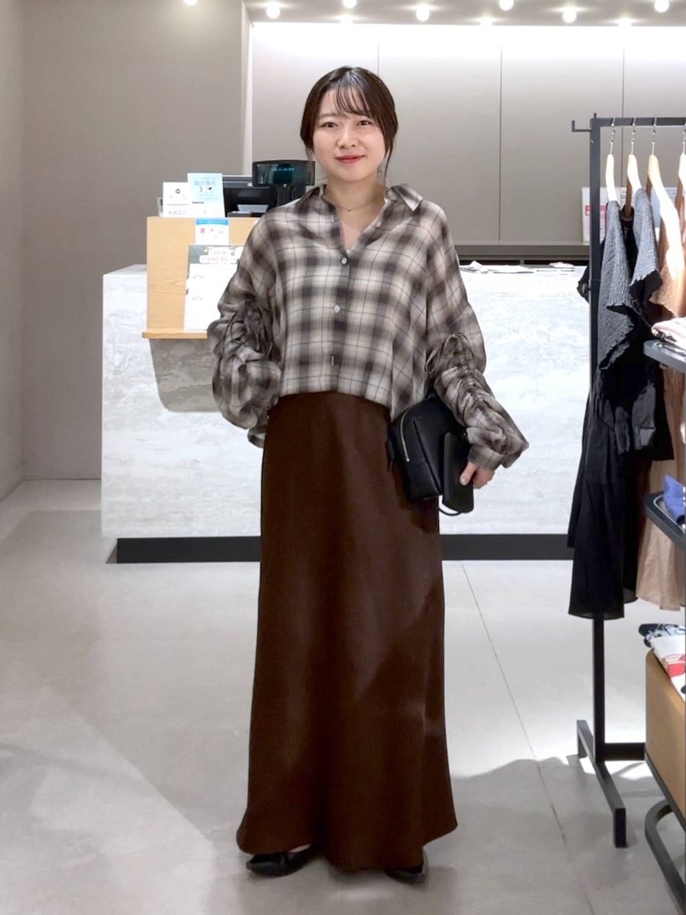 ブラウン系のスカート、ブラック系のパンプス、ブラック系のトートバッグを着用したレディースの春コーディネートの1枚目の写真