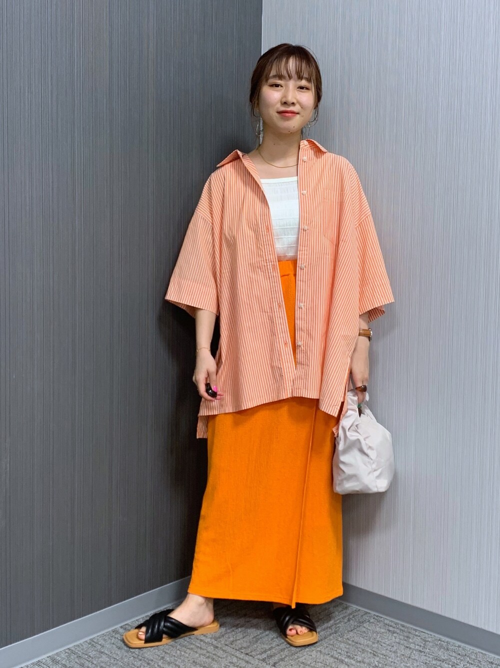 オレンジ系のシャツ/ブラウス、オレンジ系のスカート、ホワイト系のショルダーバッグを着用したレディースの夏コーディネートの2枚目の写真