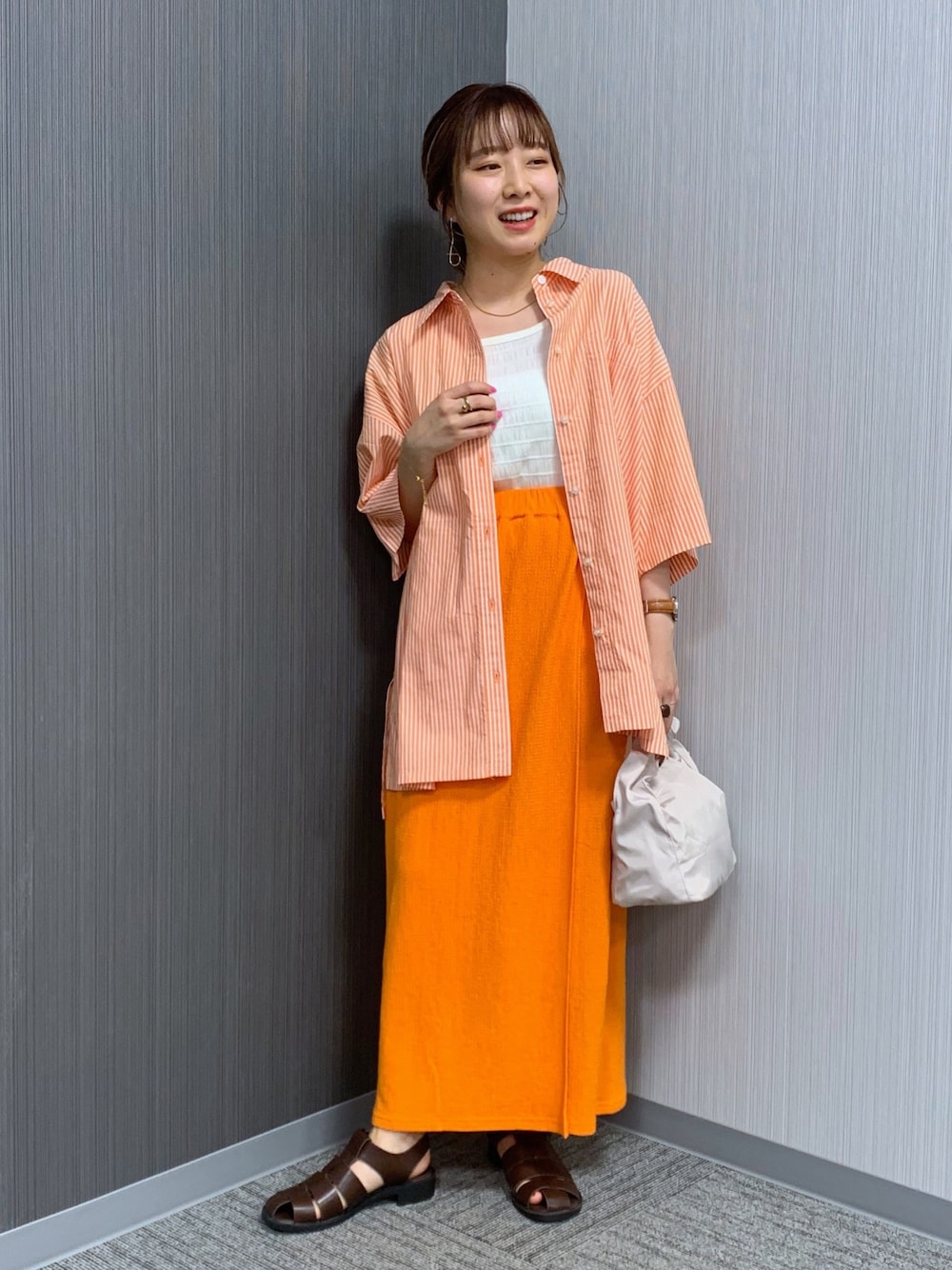 オレンジ系のシャツ/ブラウス、オレンジ系のスカート、ホワイト系のショルダーバッグを着用したレディースの夏コーディネートの3枚目の写真