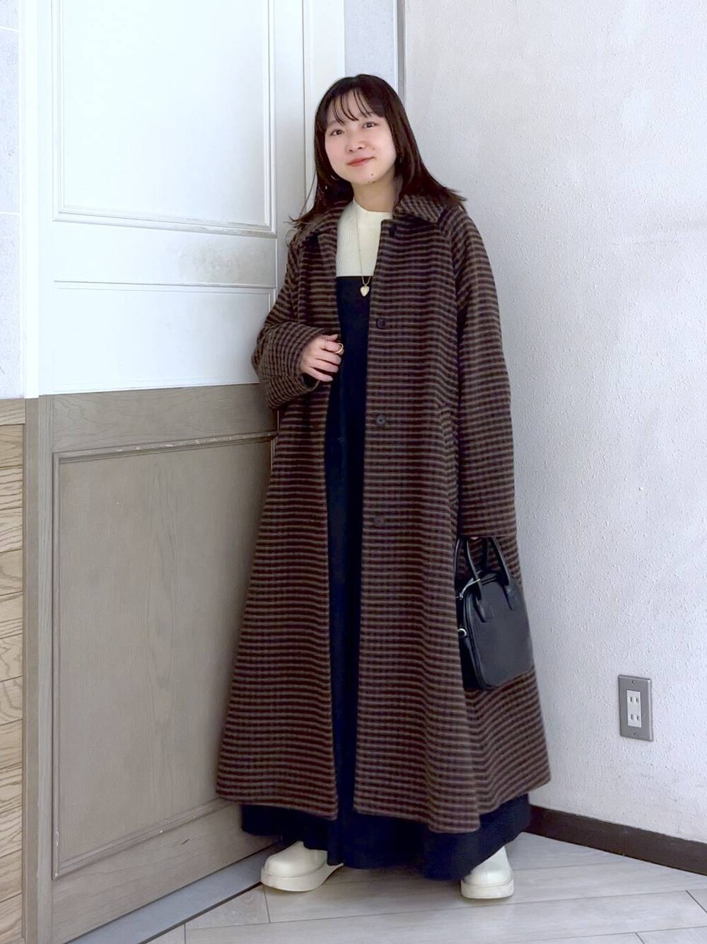 ブラウン系のノーカラーコート、ホワイト系のブーツ、ブラック系のワンピースを着用したレディースの冬コーディネートの1枚目の写真