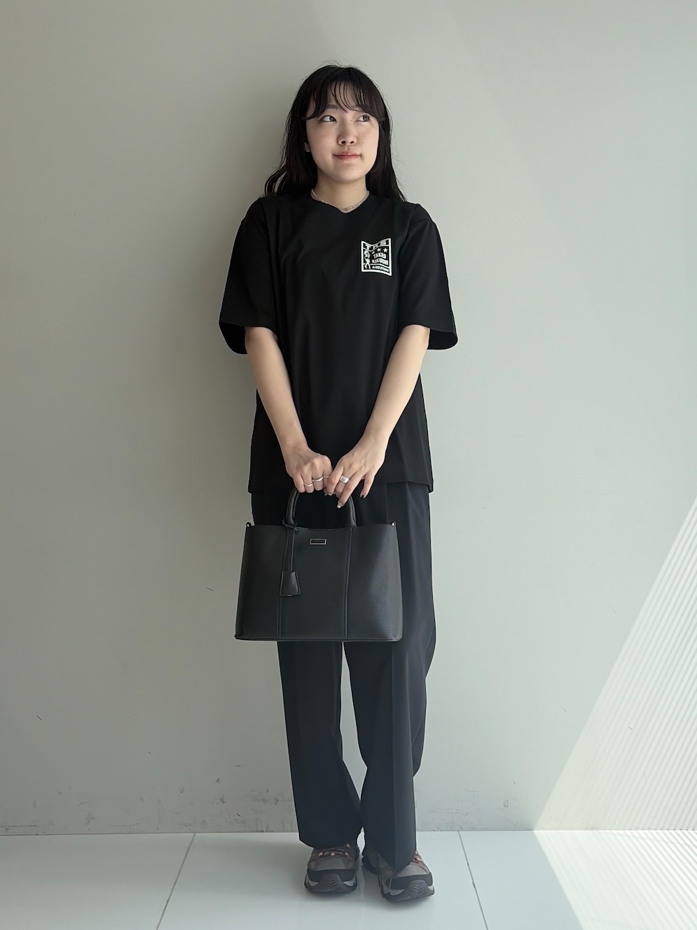 ブルー系のスラックス、ブラック系のトートバッグ、ブラック系のTシャツ/カットソーを着用したメンズの春コーディネートの1枚目の写真