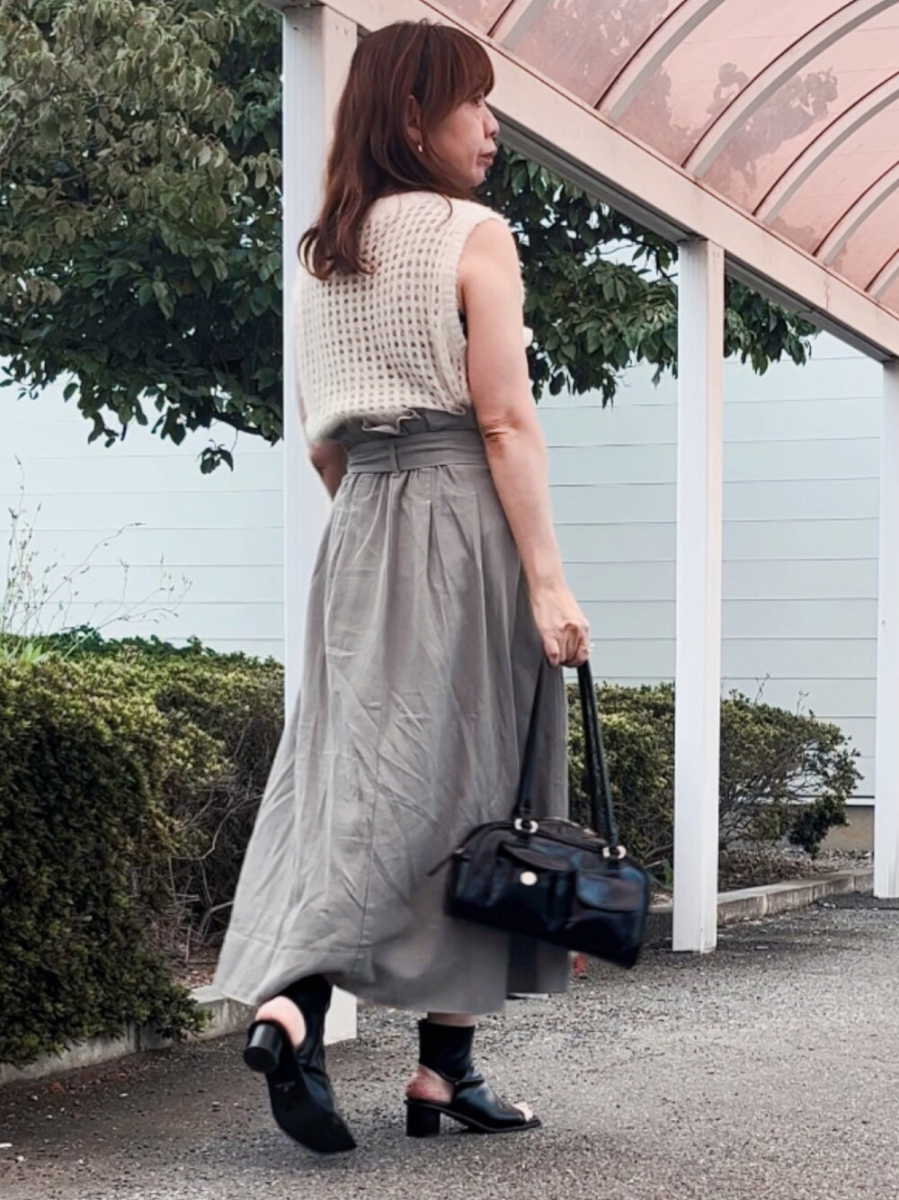 グレー系のデニムスカート、ブラック系のショルダーバッグ、ブラック系のブーツを着用したレディースの秋コーディネートの1枚目の写真