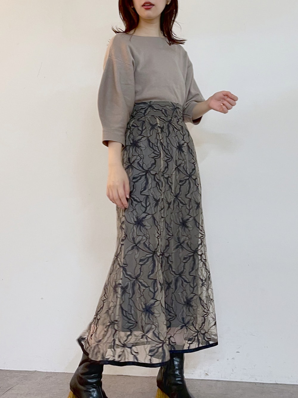 ベージュ系のニット/セーター、ブルー系のスカート、ブラック系のブーツを着用したレディースの夏コーディネートの1枚目の写真