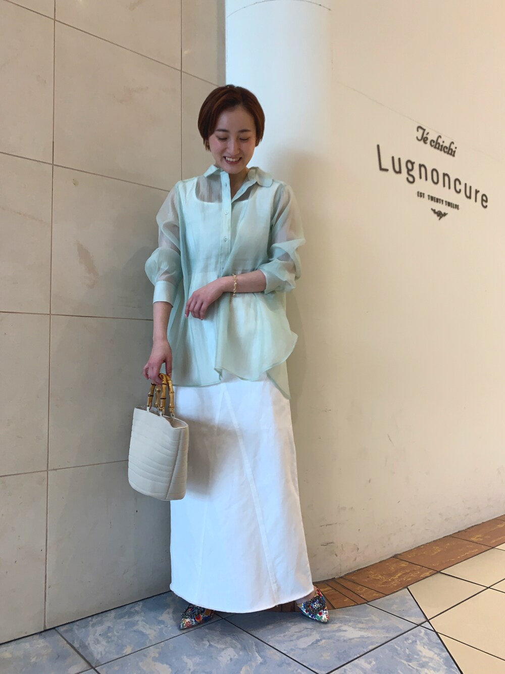 グリーン系のシャツ/ブラウス、ホワイト系のスカート、ホワイト系のパンプスを着用したレディースの春コーディネートの1枚目の写真