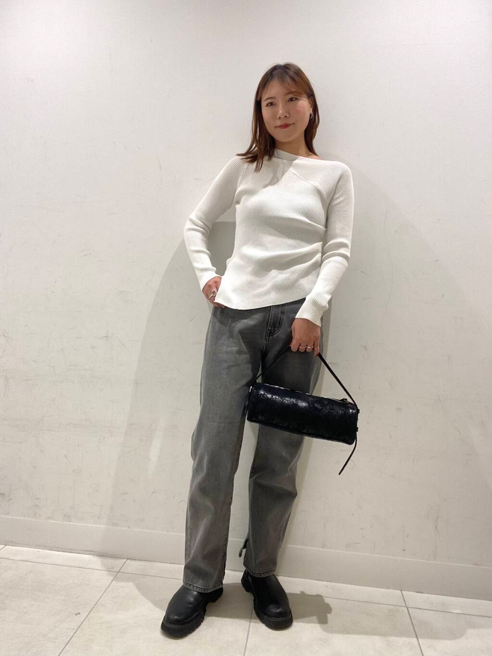 グレー系のデニムパンツ、ブラック系のハンドバッグ、ホワイト系のニット/セーターを着用したレディースの冬コーディネートの1枚目の写真