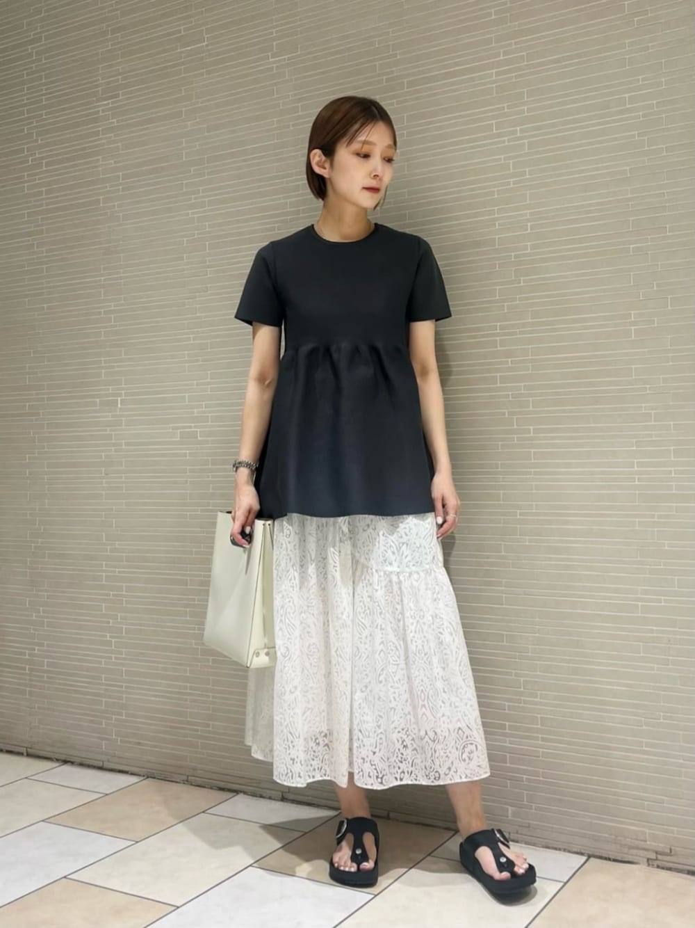 ブラック系のサンダル、ホワイト系のスカート、グレー系のニット/セーターを着用したレディースの春コーディネートの1枚目の写真