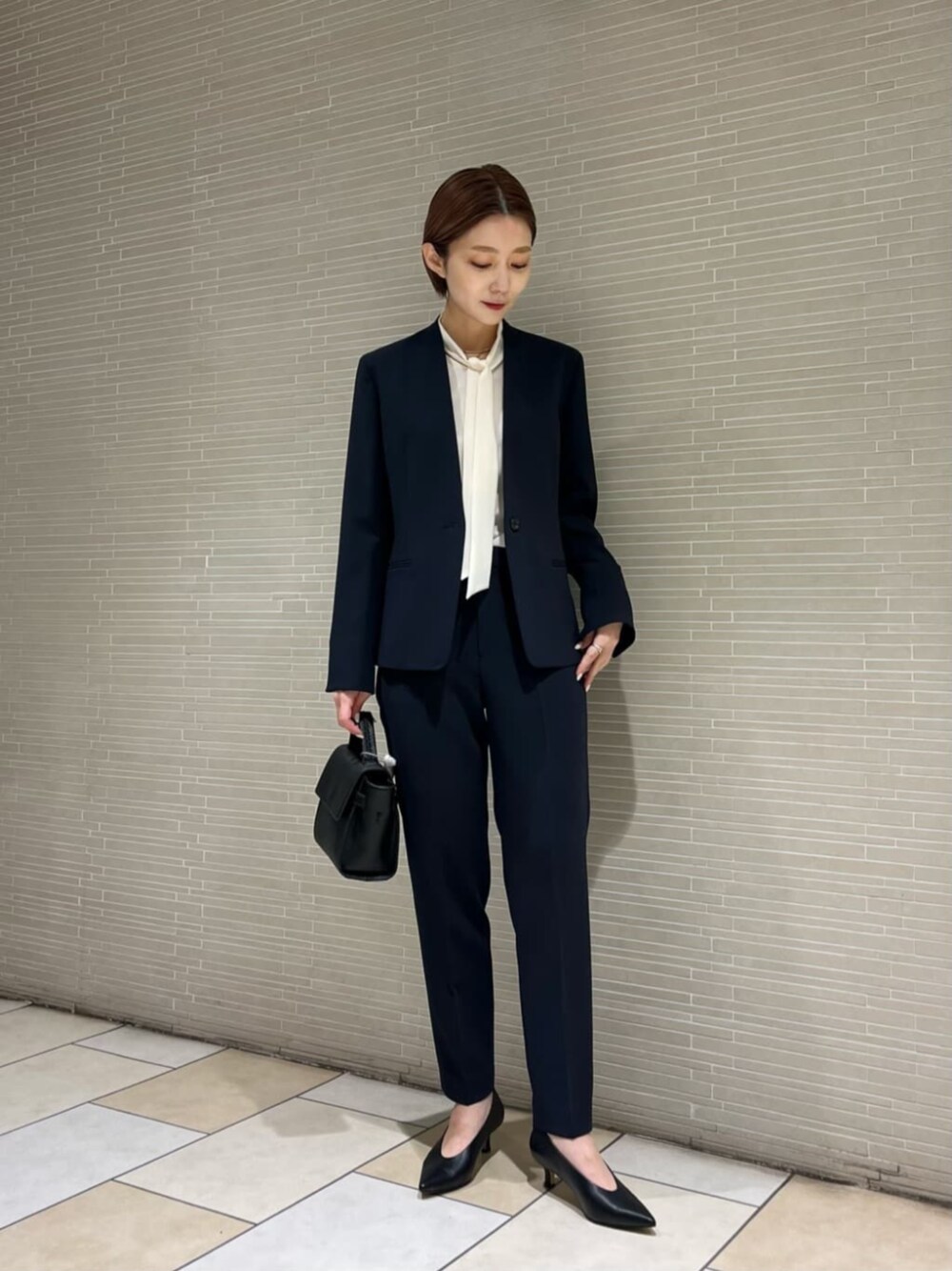 ブラック系のパンプス、ブラック系のショルダーバッグ、ブルー系のスラックスを着用したレディースの冬コーディネートの1枚目の写真