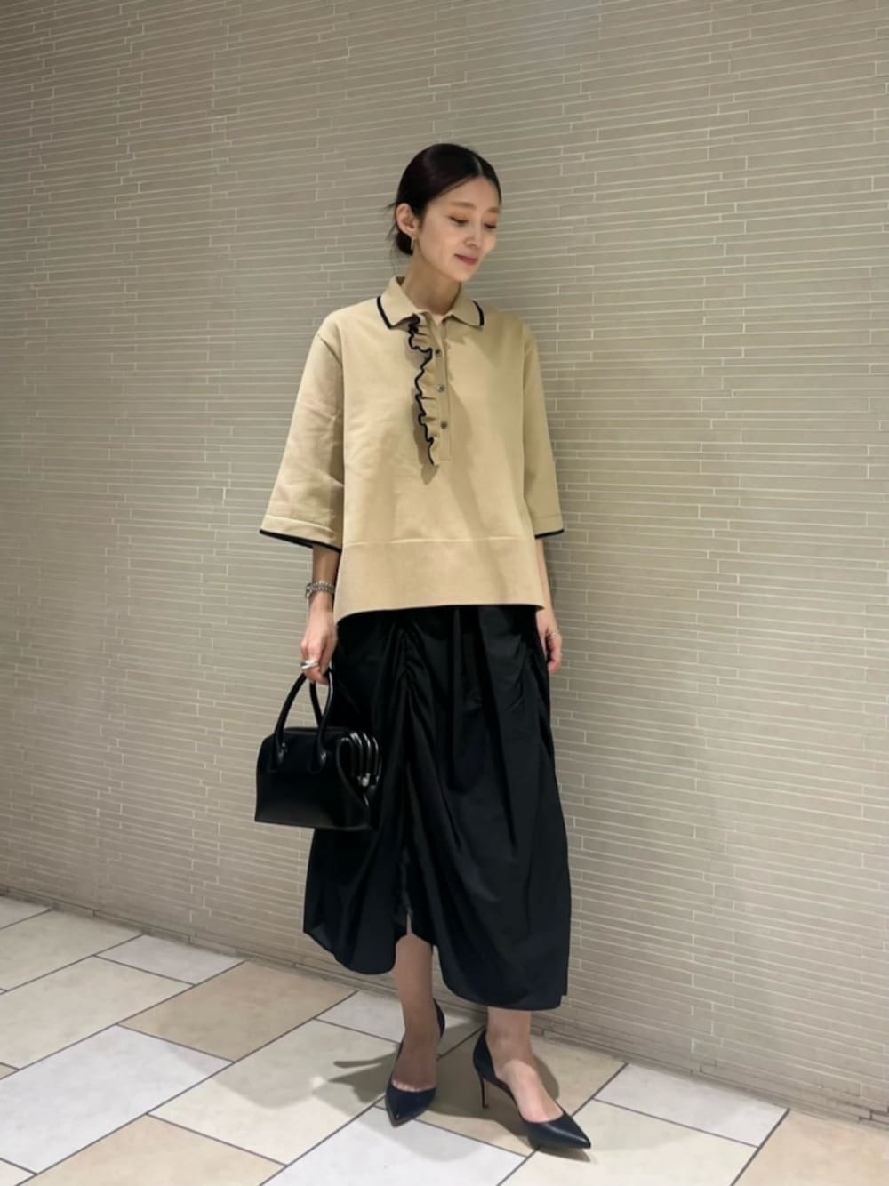 ブラック系のパンプス、ベージュ系のニット/セーター、ブラック系のスカートを着用したレディースの春コーディネートの1枚目の写真