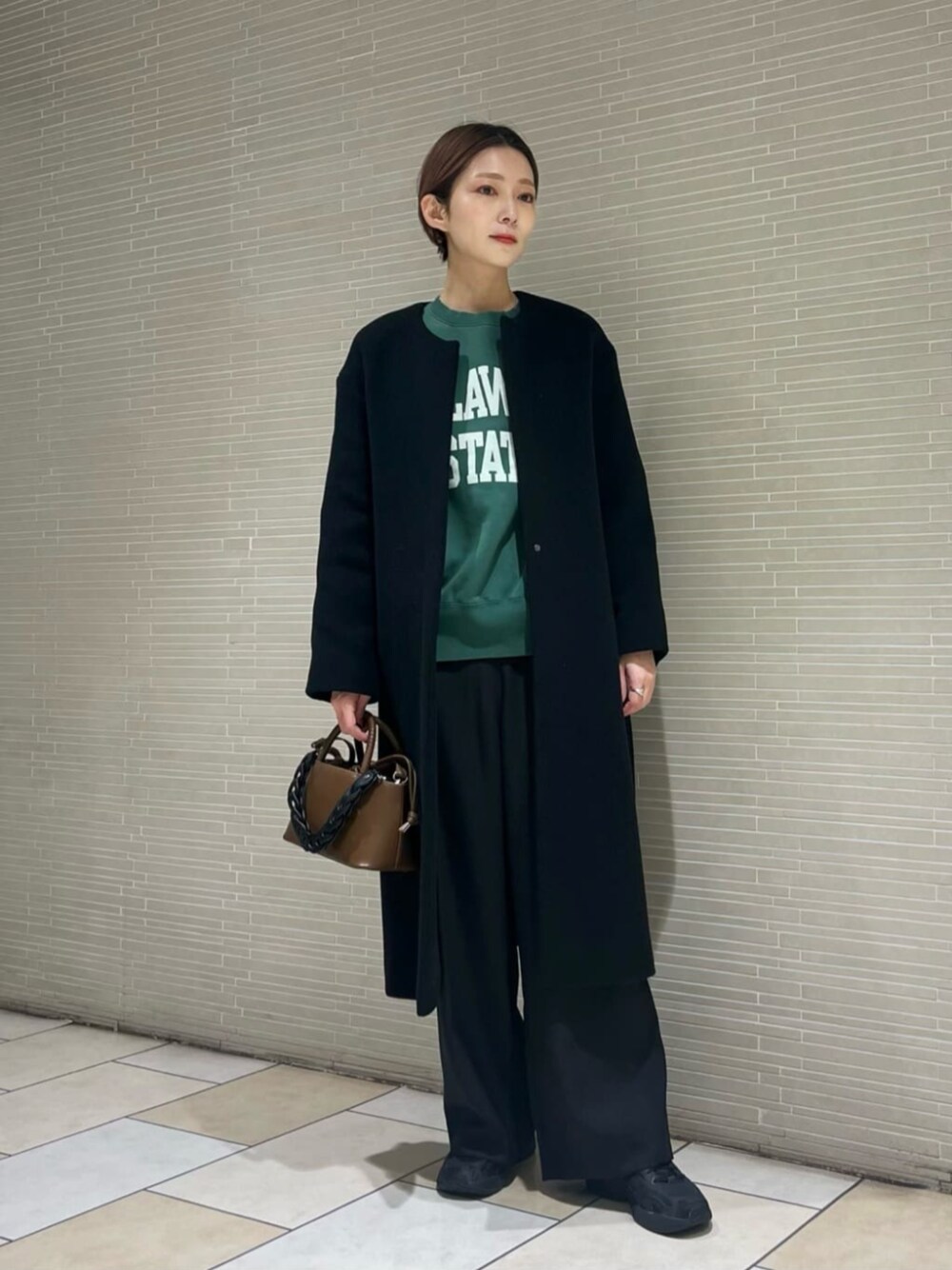 ブラウン系のショルダーバッグ、ブラック系のノーカラーコート、グリーン系のTシャツ/カットソーを着用したレディースの冬コーディネートの1枚目の写真
