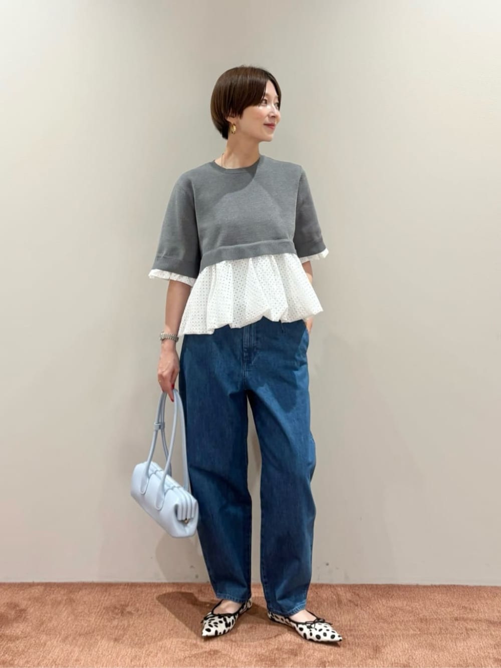 グレー系のニット/セーター、ブルー系のデニムパンツ、ブルー系のショルダーバッグを着用したレディースの夏コーディネートの1枚目の写真