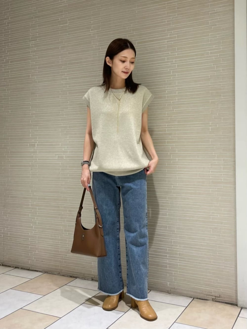 ゴールド系のニット/セーター、ブルー系のデニムパンツ、ベージュ系のブーツを着用したレディースの夏コーディネートの1枚目の写真