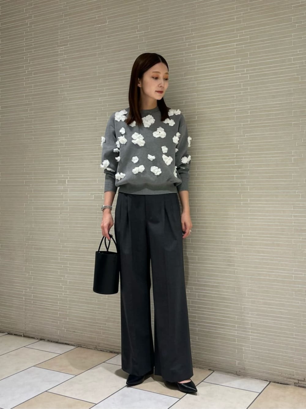 グレー系のニット/セーター、グレー系のスラックス、ブラック系のトートバッグを着用したレディースの秋コーディネートの1枚目の写真