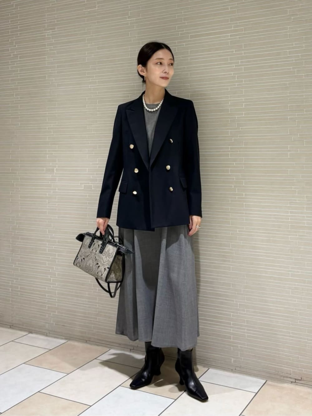 グレー系のワンピース、ブラック系のブーツ、ブラック系のトートバッグを着用したレディースの秋コーディネートの1枚目の写真