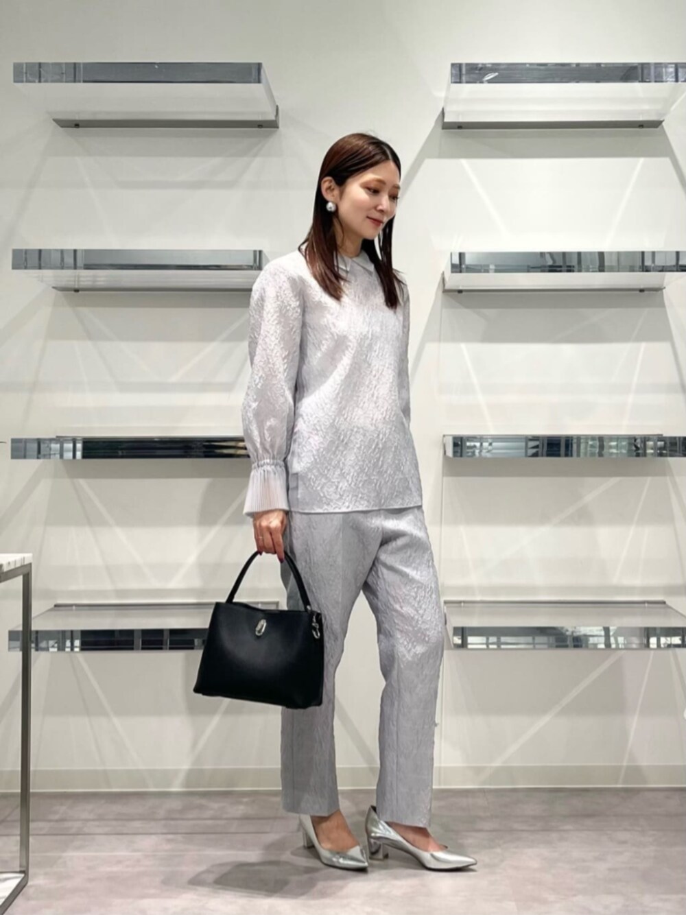 シルバー系のパンプス、ブラック系のショルダーバッグ、グレー系のシャツ/ブラウスを着用したレディースの秋コーディネートの1枚目の写真