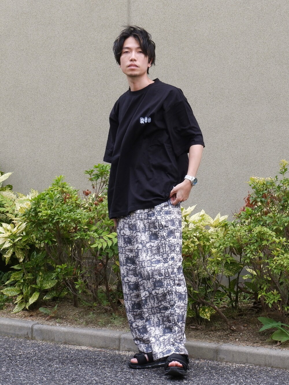 ブラック系のTシャツ/カットソー、ホワイト系のスラックス、ブラック系のサンダルを着用したメンズの夏コーディネートの1枚目の写真