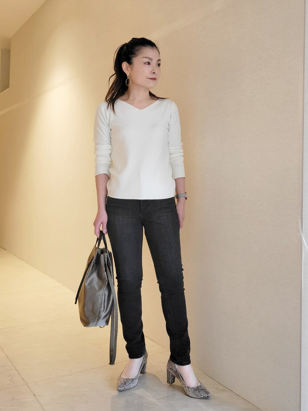 ホワイト系のニット/セーター、ブラック系のデニムパンツ、ベージュ系のトートバッグを着用したレディースの冬コーディネートの1枚目の写真