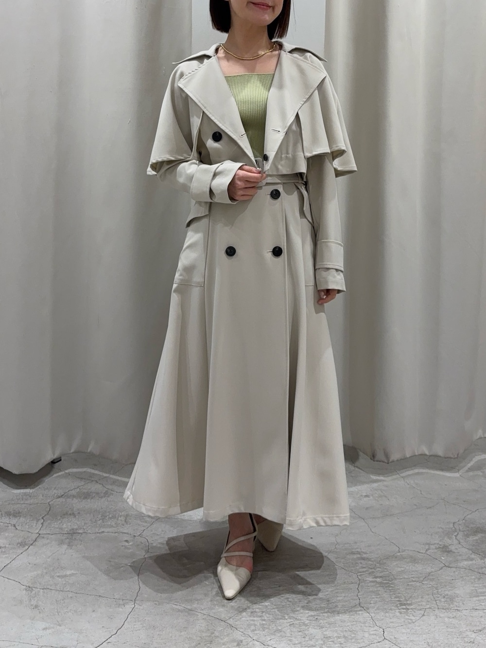 ホワイト系のトレンチコート、グリーン系のニット/セーター、ホワイト系のパンプスを着用したレディースの冬コーディネートの1枚目の写真