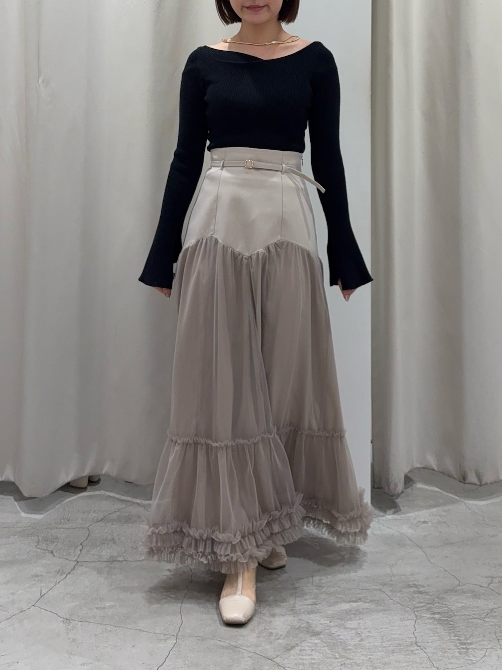 ベージュ系のスカート、ブラック系のニット/セーターを着用したレディースの春コーディネートの1枚目の写真