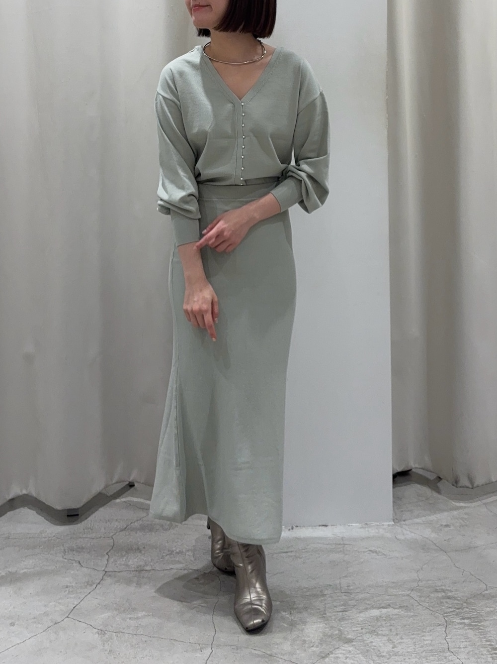 グリーン系のニット/セーター、グリーン系のスカート、シルバー系のブーツを着用したレディースの冬コーディネートの1枚目の写真