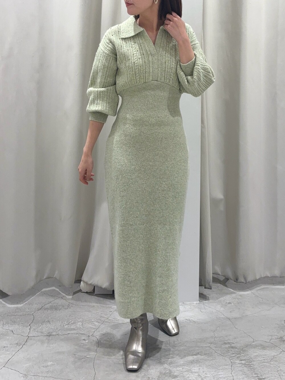 グリーン系のワンピース、シルバー系のブーツ、ゴールド系のイヤリングを着用したレディースの秋コーディネートの1枚目の写真