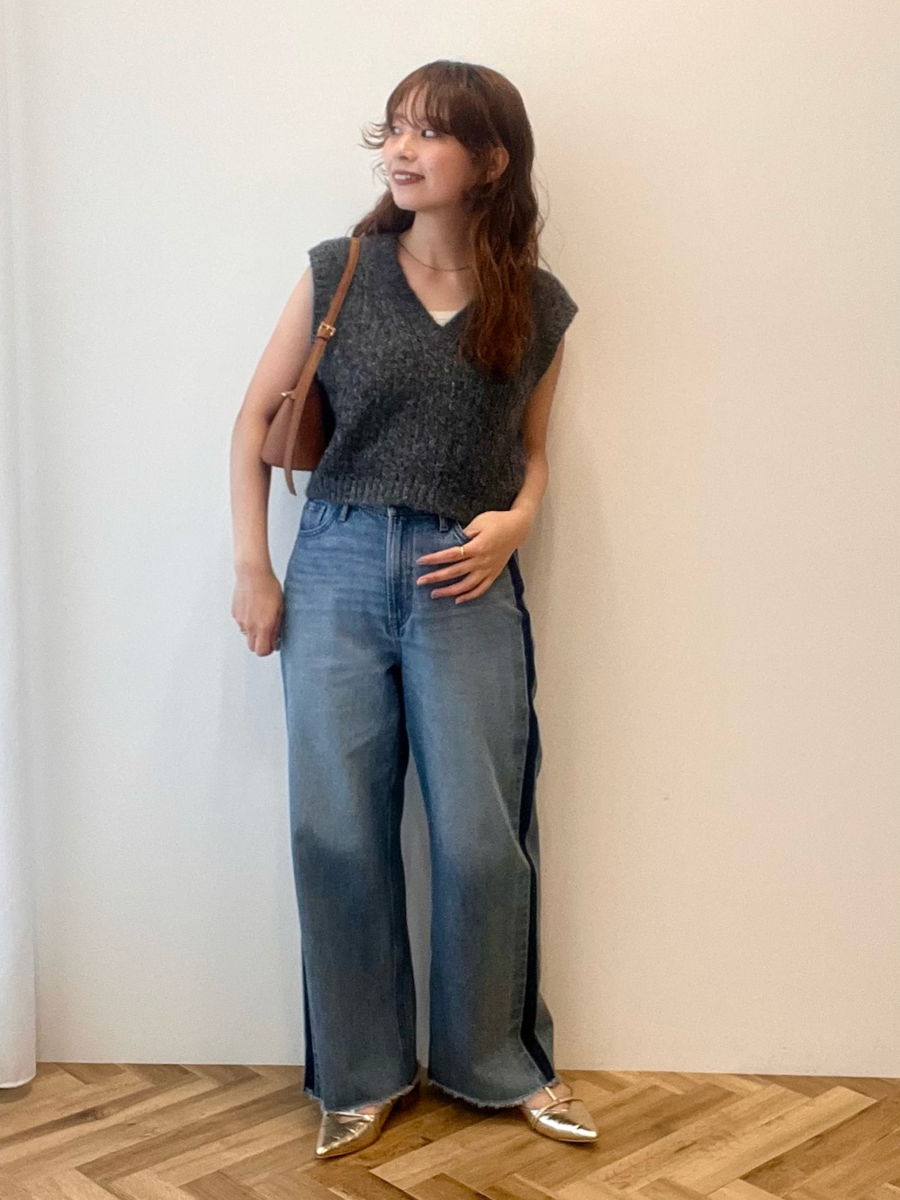 グレー系のベスト、ブルー系のデニムパンツ、ブラウン系のショルダーバッグを着用したレディースの秋コーディネートの1枚目の写真