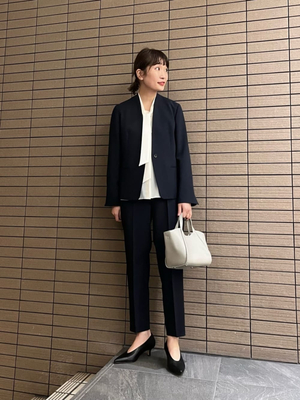 ブルー系のノーカラージャケット、ブラック系のパンプス、ホワイト系のシャツ/ブラウスを着用したレディースの春コーディネートの1枚目の写真