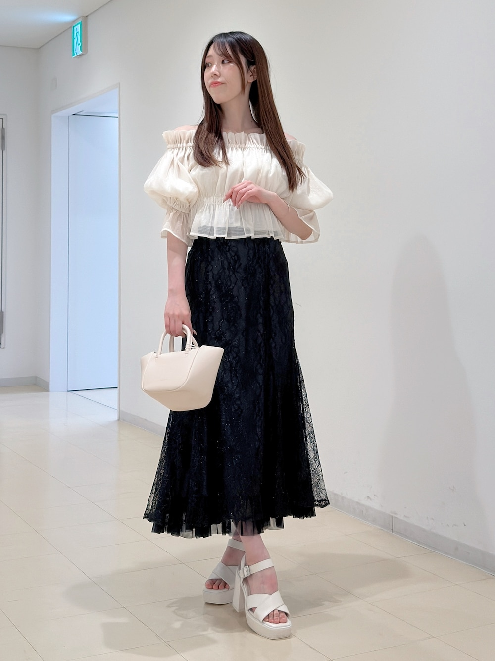 ホワイト系のシャツ/ブラウス、ブラック系のスカート、ホワイト系のサンダルを着用したレディースの春コーディネートの1枚目の写真