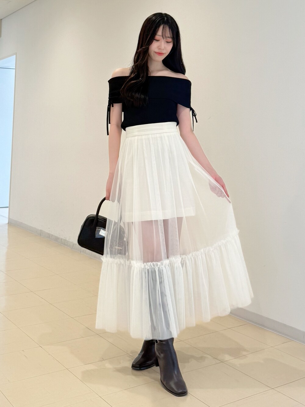 ブラック系のニット/セーター、ホワイト系のスカート、ブラック系のハンドバッグを着用したレディースの夏コーディネートの1枚目の写真