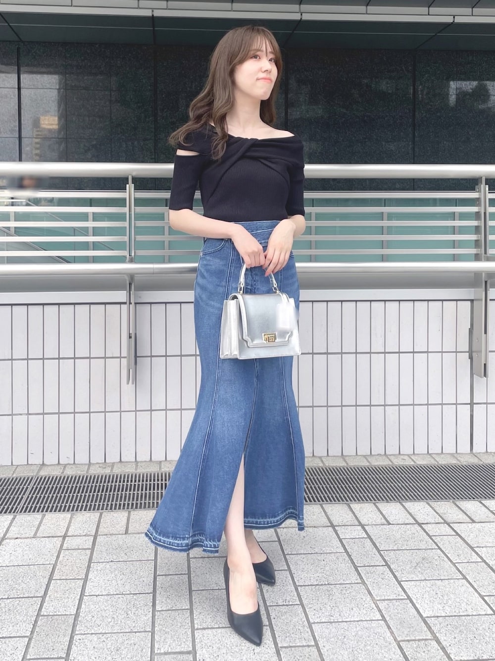 ブラック系のニット/セーター、ブルー系のデニムスカート、シルバー系のハンドバッグを着用したレディースの夏コーディネートの1枚目の写真