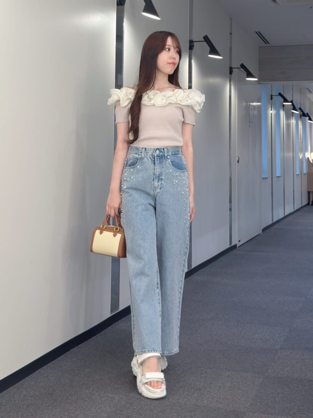 ブラウン系のハンドバッグ、ブルー系のデニムパンツ、ホワイト系のサンダルを着用したレディースの夏コーディネートの1枚目の写真
