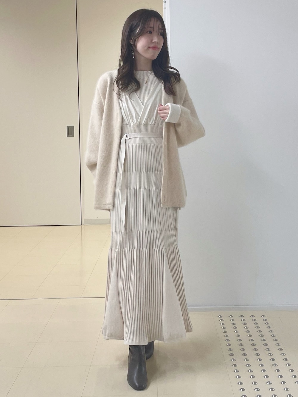ベージュ系のカーディガン/ボレロ、ブラウン系のブーツ、ホワイト系のワンピースを着用したレディースの冬コーディネートの1枚目の写真