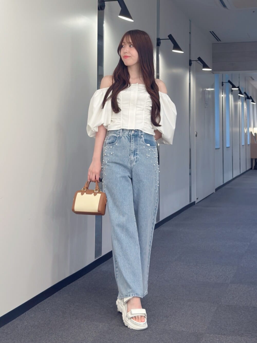 ブラウン系のハンドバッグ、ブルー系のデニムパンツ、ホワイト系のサンダルを着用したレディースの夏コーディネートの1枚目の写真