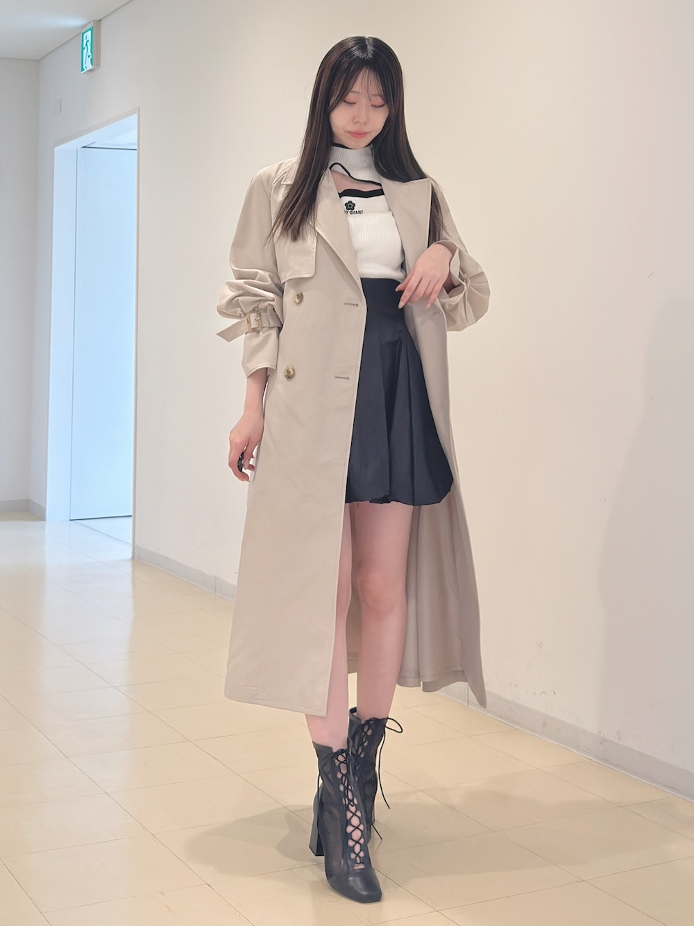 ベージュ系のトレンチコート、ホワイト系のニット/セーター、ブラック系のスカートを着用したレディースの春コーディネートの1枚目の写真