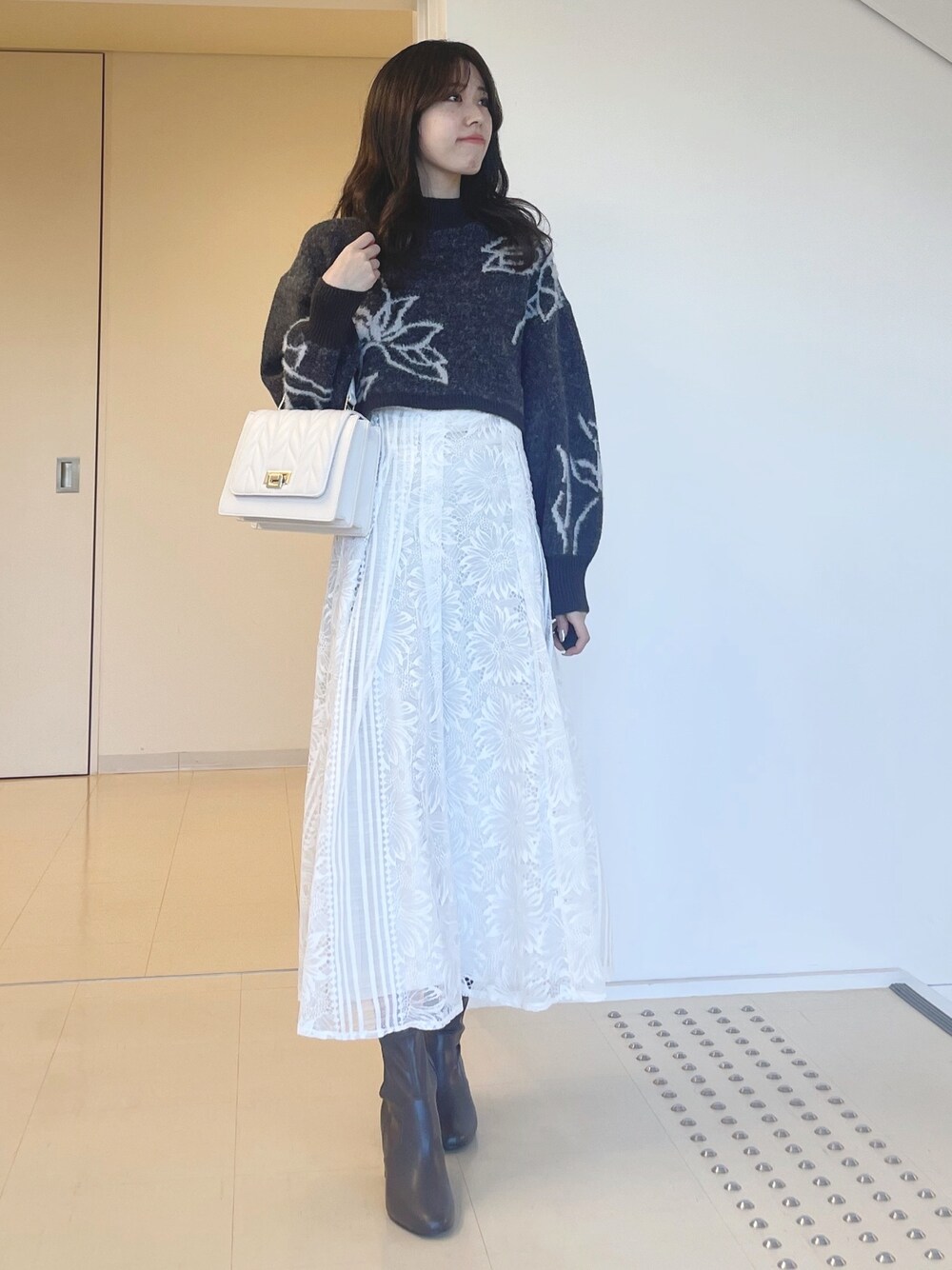 グレー系のニット/セーター、ホワイト系のスカート、ホワイト系のショルダーバッグを着用したレディースの秋コーディネートの1枚目の写真