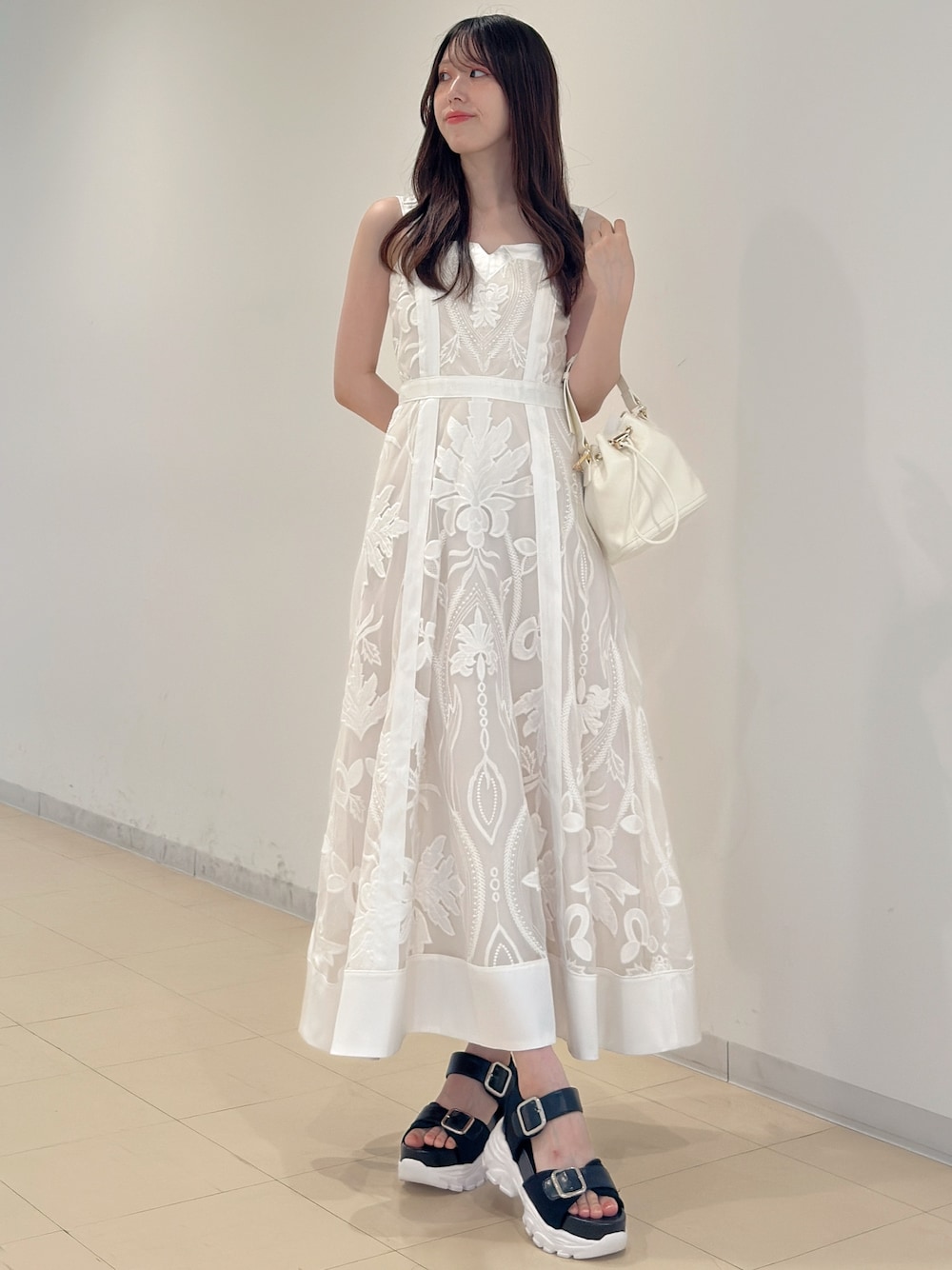 ホワイト系のワンピース、ホワイト系のハンドバッグ、ブラック系のサンダルを着用したレディースの夏コーディネートの1枚目の写真