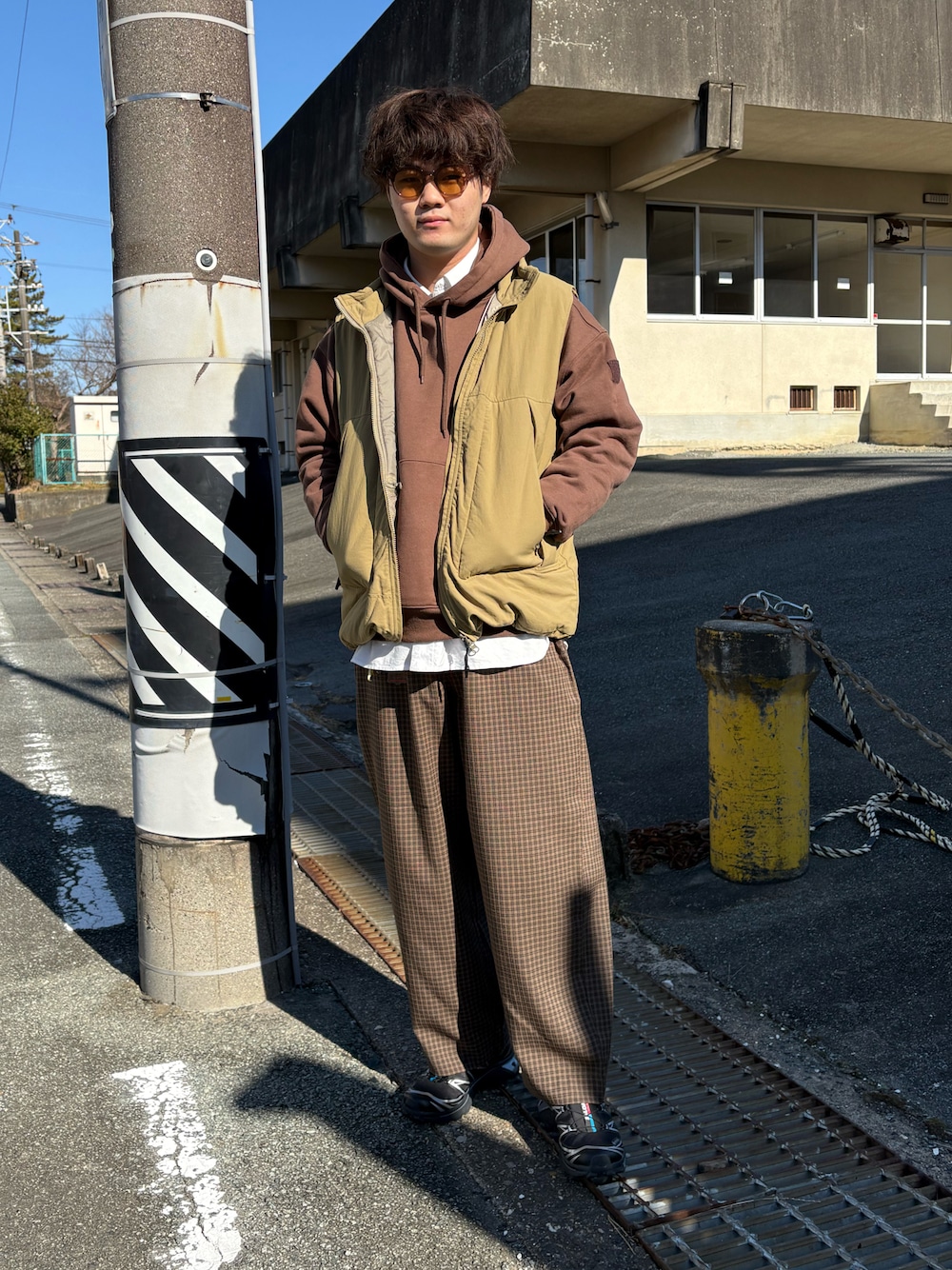 ブラック系のスニーカー、ブラウン系のパンツ、ベージュ系のダウンベストを着用したメンズの冬コーディネートの1枚目の写真