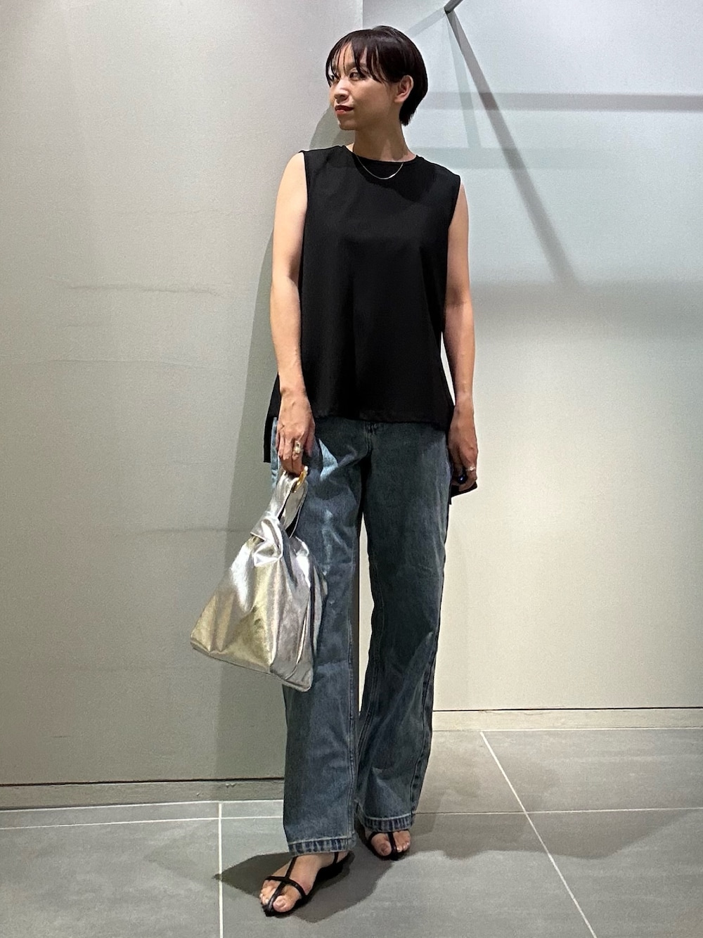 ブルー系のデニムパンツ、シルバー系のハンドバッグ、ブラック系のタンクトップを着用したレディースの夏コーディネートの1枚目の写真