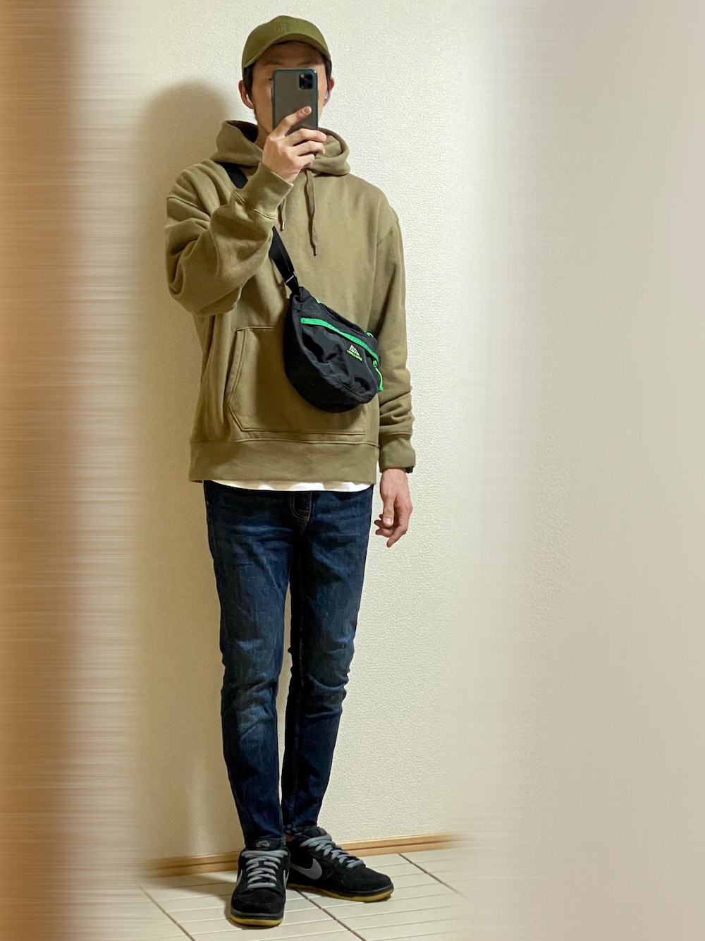 ブラック系のスニーカー、ブルー系のデニムパンツ、グリーン系のパーカーを着用したメンズの秋コーディネートの1枚目の写真