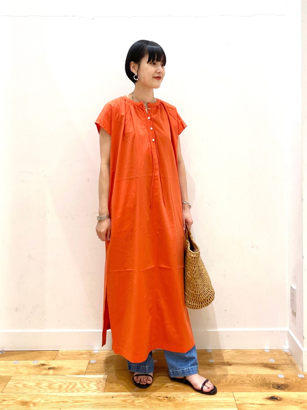 オレンジ系のワンピース、ブルー系のデニムパンツ、ベージュ系のトートバッグを着用したレディースの夏コーディネートの1枚目の写真