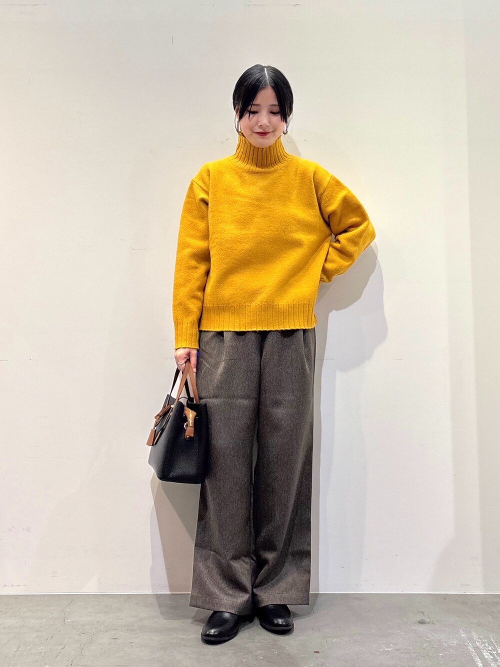 イエロー系のニット/セーター、ブラウン系のその他パンツ、ブラック系のトートバッグを着用したレディースの冬コーディネートの1枚目の写真
