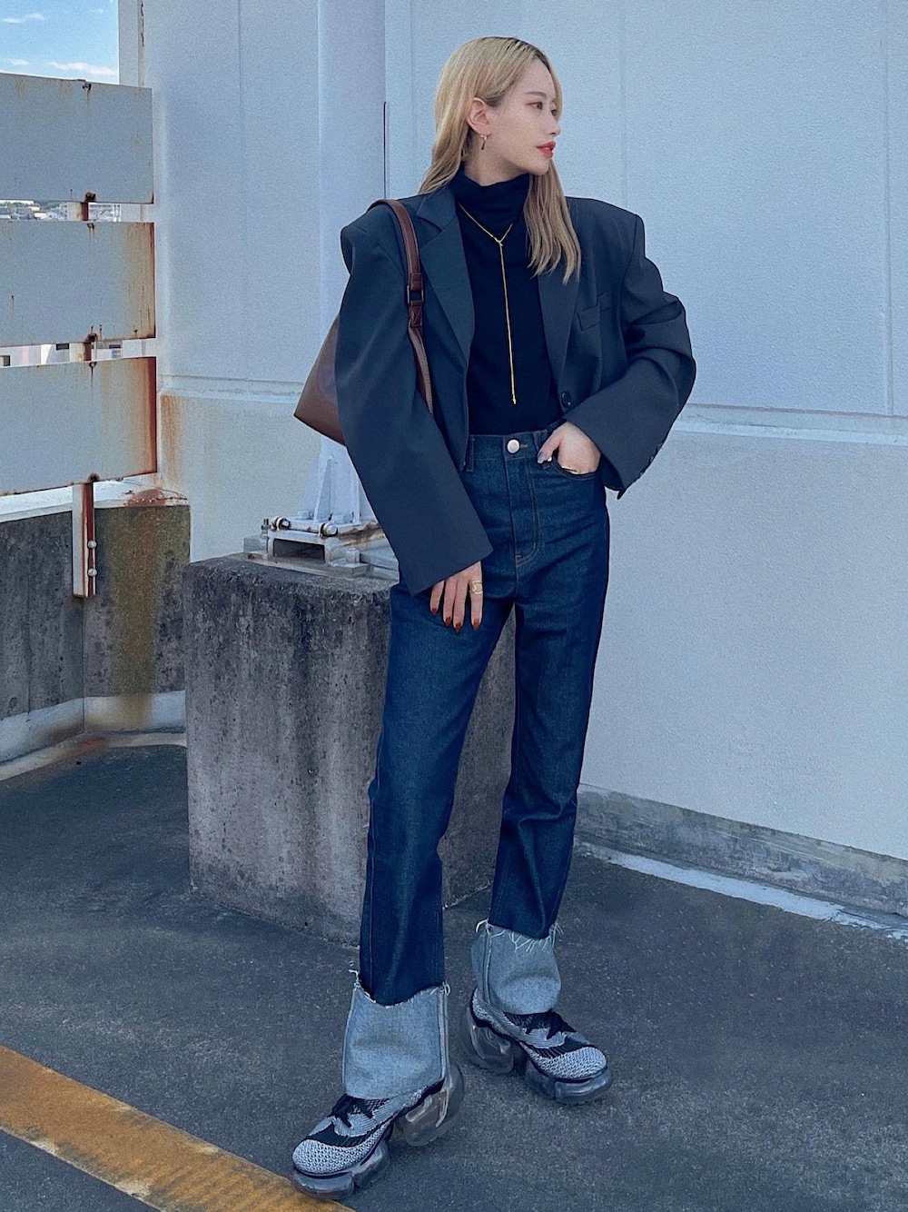 ブラウン系のハンドバッグ、ブルー系のデニムパンツ、ブラック系のスニーカーを着用したレディースの秋コーディネートの1枚目の写真