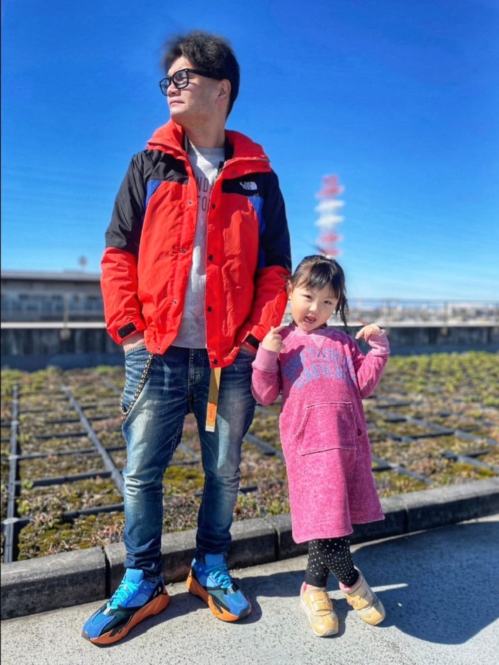 レッド系のナイロンジャケット、ブルー系のデニムパンツ、ブルー系のスニーカーを着用したメンズの春コーディネートの1枚目の写真