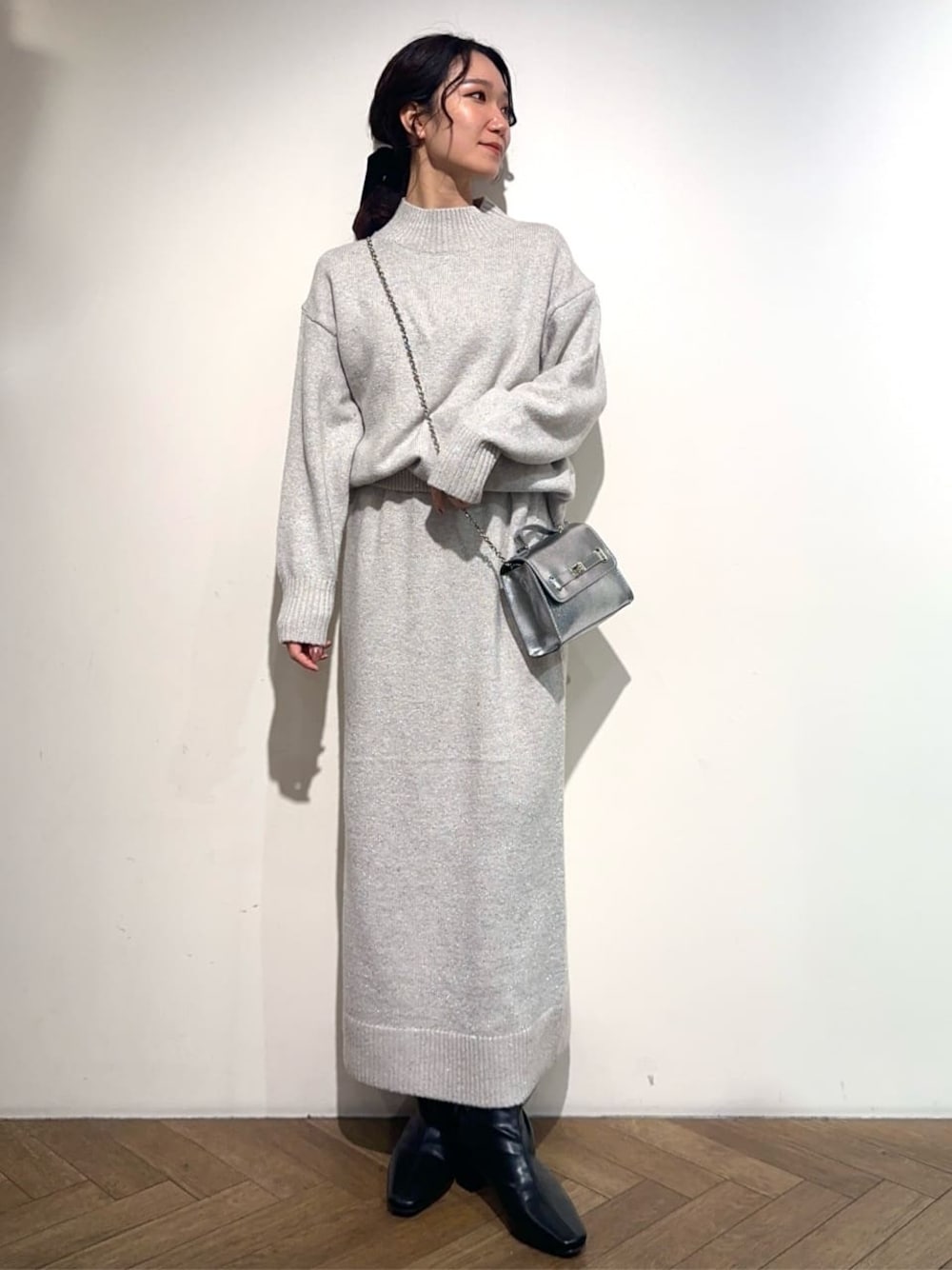 グレー系のニット/セーター、グレー系のスカート、シルバー系のショルダーバッグを着用したレディースの冬コーディネートの1枚目の写真