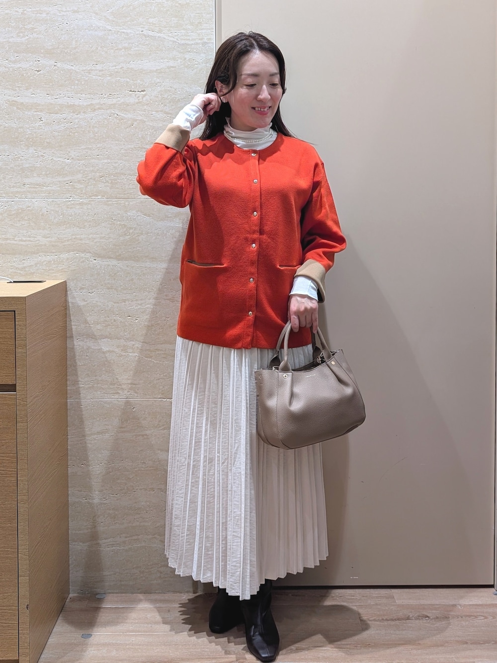 オレンジ系のカーディガン/ボレロ、ホワイト系のスカート、ベージュ系のトートバッグを着用したレディースの秋コーディネートの1枚目の写真
